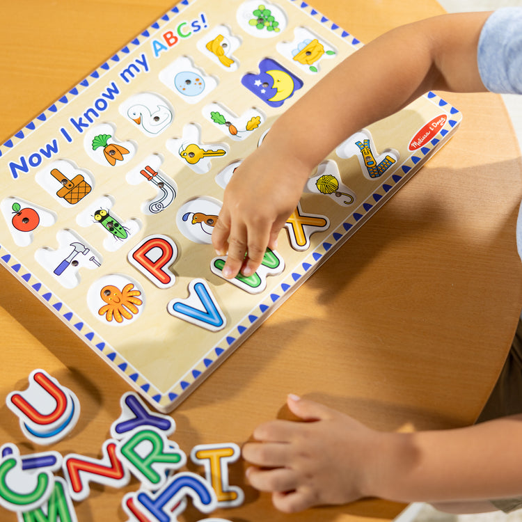 A kid playing with The Melissa & Doug Wooden Alphabet Sound Puzzle - Wooden Puzzle With Light-Activated Sound Effects (26 pcs)