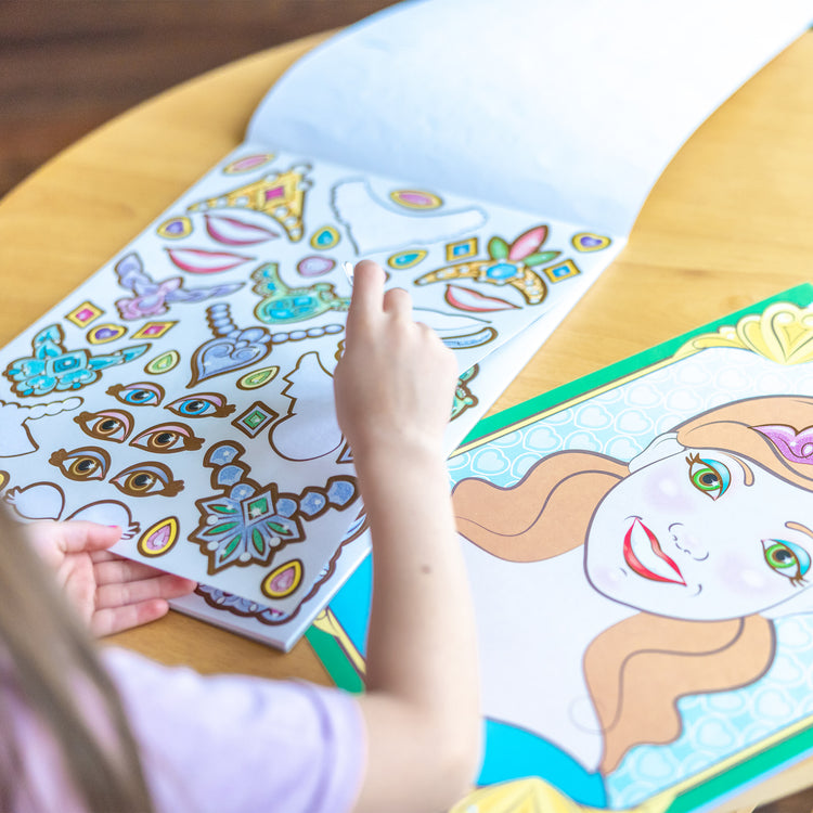 A kid playing with The Melissa & Doug Make-a-Face Sticker Pad: Sparkling Princesses - 15 Faces, 4 Sticker Sheets