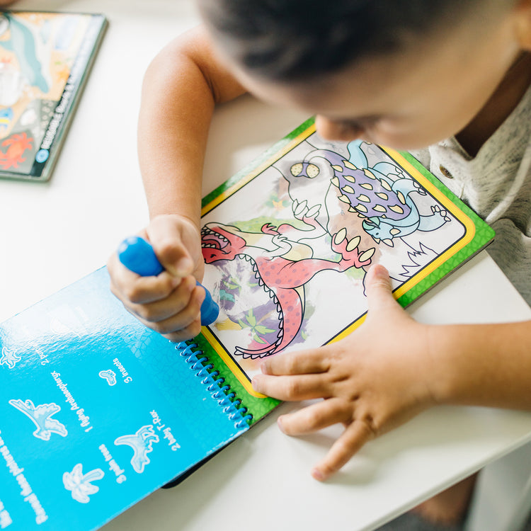 A kid playing with The Melissa & Doug Water WOW! 3-Pack – Dinosaur, Adventure, Space Water-Reveal Travel Activity Pads