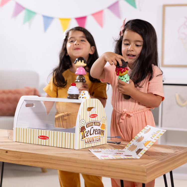 A kid playing with The Melissa & Doug Wooden Scoop and Serve Ice Cream Counter With Play Food and Accessories (28 Pcs)