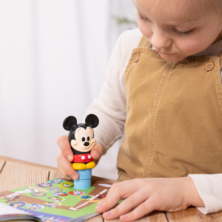 A kid playing with The Melissa & Doug Sticker WOW!™ Disney Mickey Mouse Bundle: 24-Page Activity Pad, Sticker Stamper, 500 Stickers, Mini Pad, Arts and Crafts Fidget Toy Collectible Character