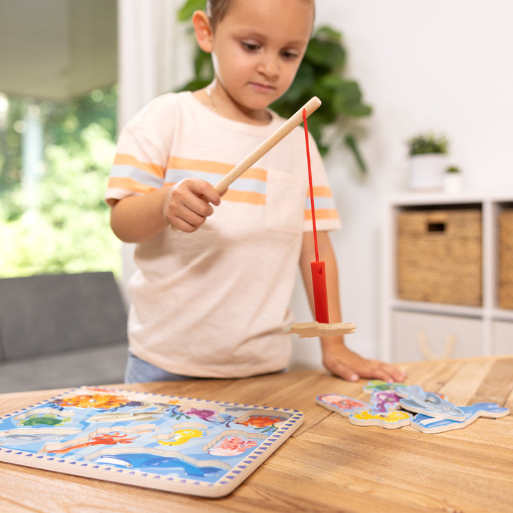 A kid playing with The Melissa & Doug Magnetic Wooden Fishing Game and Puzzle With Wooden Ocean Animal Magnets