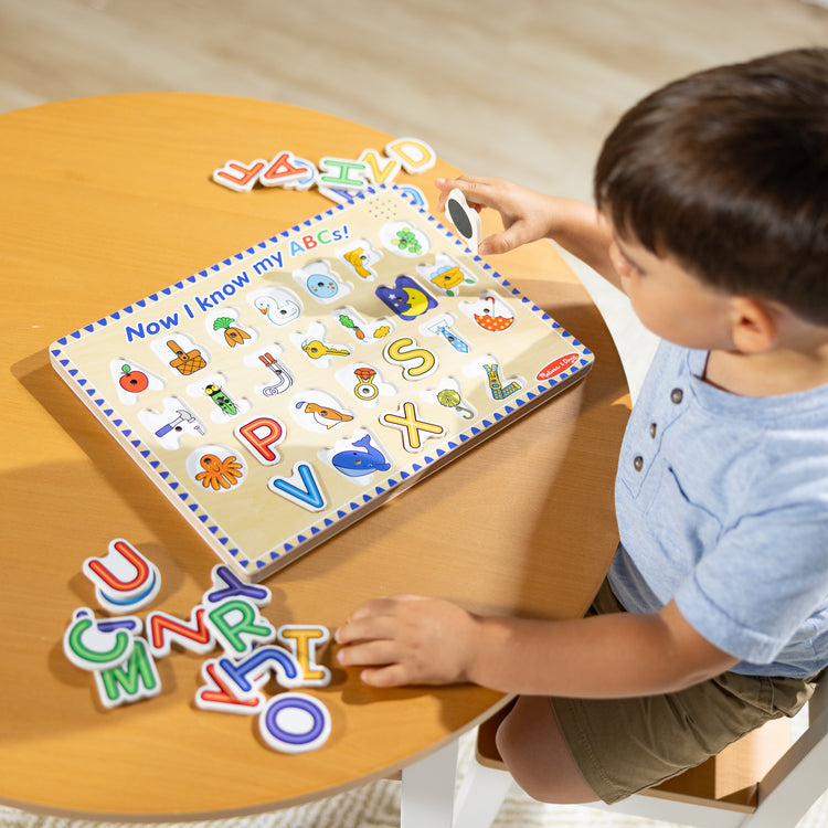 A kid playing with The Melissa & Doug Wooden Alphabet Sound Puzzle - Wooden Puzzle With Light-Activated Sound Effects (26 pcs)