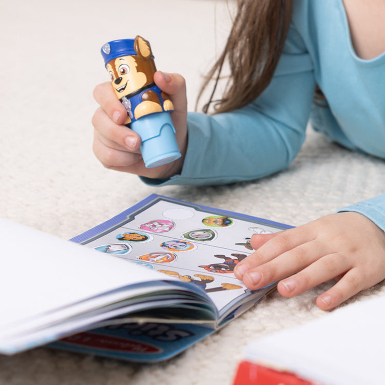A kid playing with The Melissa & Doug Sticker WOW!™ 24-Page Activity Pad and Sticker Stamper, 300 Stickers, Arts and Crafts Fidget Toy Collectible Character – PAW Patrol Chase