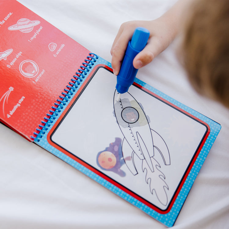 A kid playing with The Melissa & Doug Water WOW! 3-Pack – Dinosaur, Adventure, Space Water-Reveal Travel Activity Pads