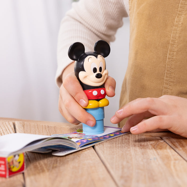 A kid playing with The Melissa & Doug Sticker WOW!™ Disney Mickey Mouse Bundle: 24-Page Activity Pad, Sticker Stamper, 500 Stickers, Mini Pad, Arts and Crafts Fidget Toy Collectible Character