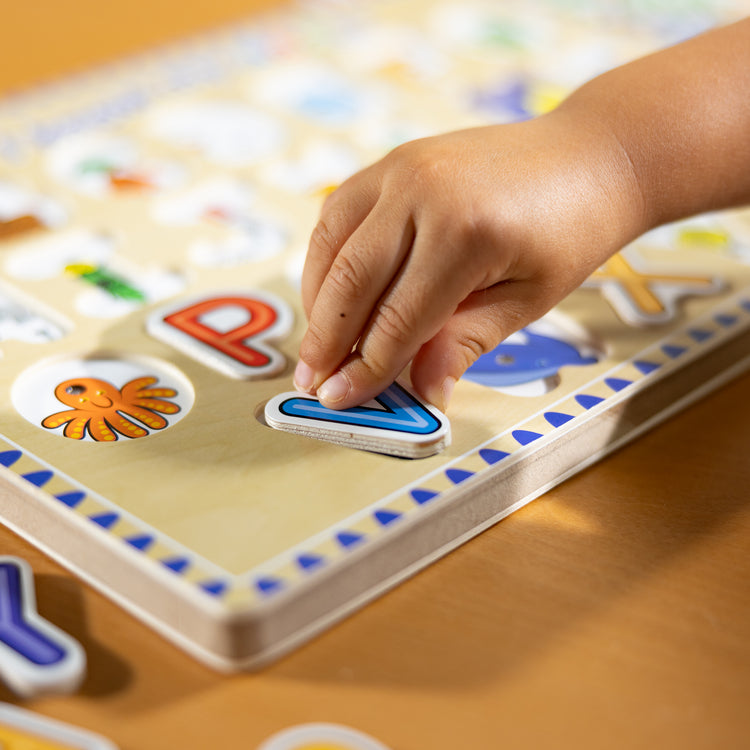 A kid playing with The Melissa & Doug Wooden Alphabet Sound Puzzle - Wooden Puzzle With Light-Activated Sound Effects (26 pcs)