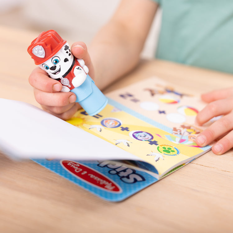 A kid playing with The Melissa & Doug Sticker WOW!™ PAW Patrol Marshall Bundle: 24-Page Activity Pad, Sticker Stamper, 500 Stickers, Mini Pad, Arts and Crafts Fidget Toy Collectible Character