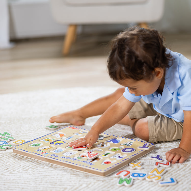 A kid playing with The Melissa & Doug Wooden Alphabet Sound Puzzle - Wooden Puzzle With Light-Activated Sound Effects (26 pcs)