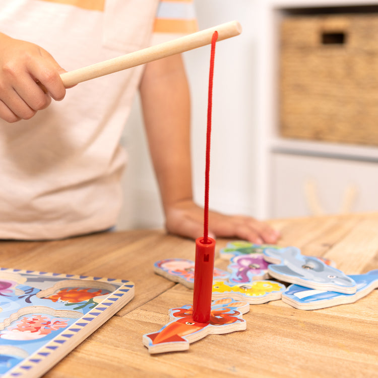A kid playing with The Melissa & Doug Magnetic Wooden Fishing Game and Puzzle With Wooden Ocean Animal Magnets