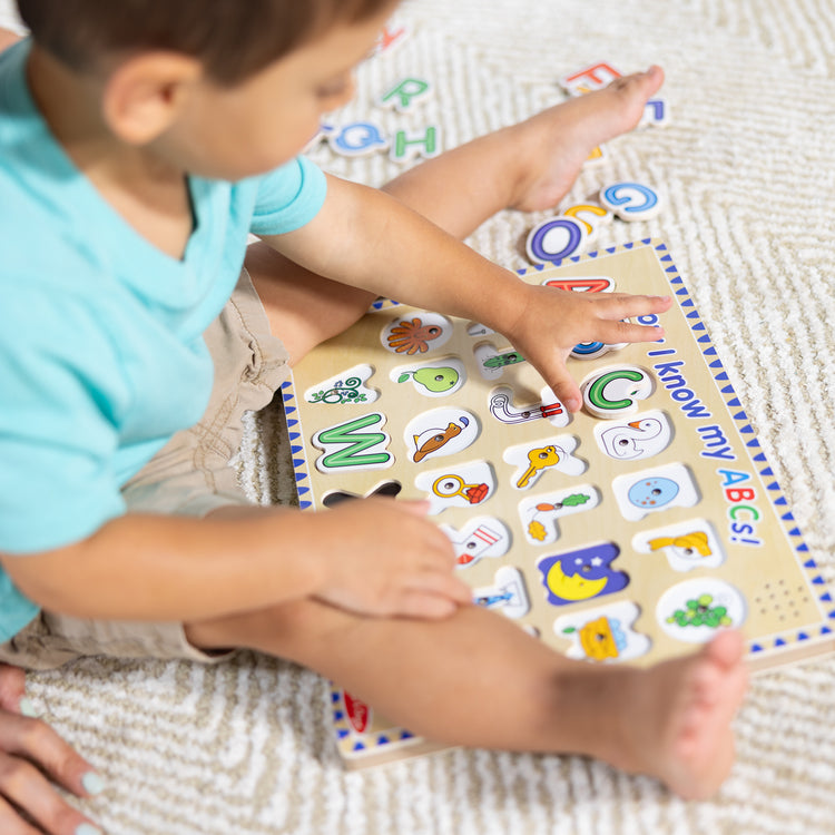 A kid playing with The Melissa & Doug Wooden Alphabet Sound Puzzle - Wooden Puzzle With Light-Activated Sound Effects (26 pcs)