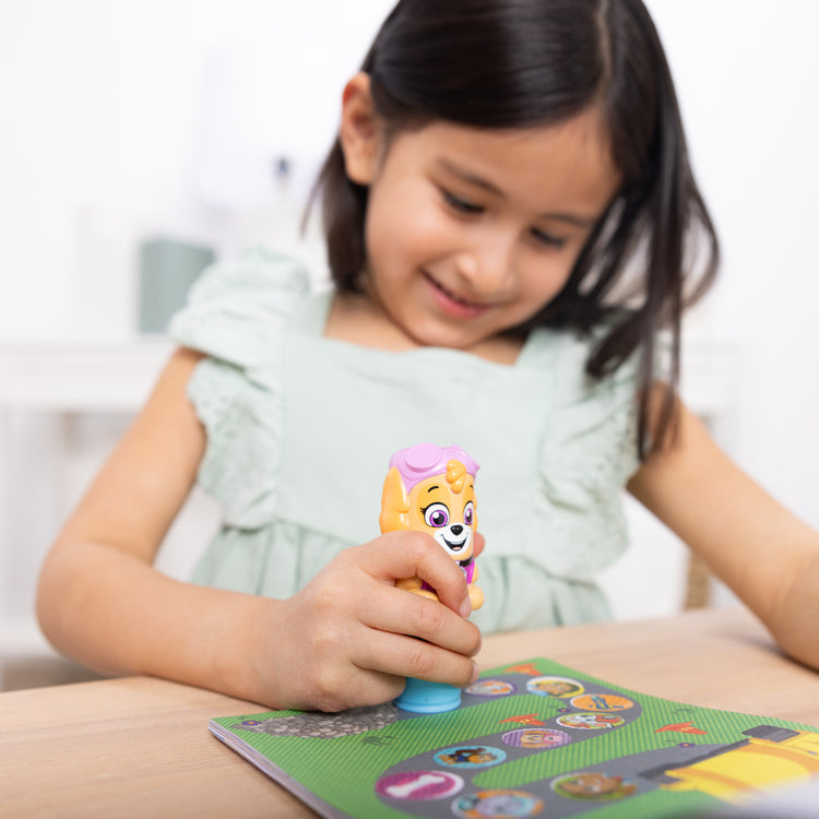 A kid playing with The Melissa & Doug Sticker WOW!™ 24-Page Activity Pad and Sticker Stamper, 300 Stickers, Arts and Crafts Fidget Toy Collectible Character – PAW Patrol Skye