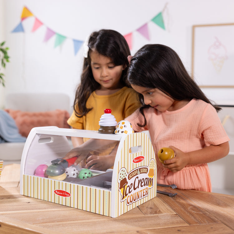 A kid playing with The Melissa & Doug Wooden Scoop and Serve Ice Cream Counter With Play Food and Accessories (28 Pcs)