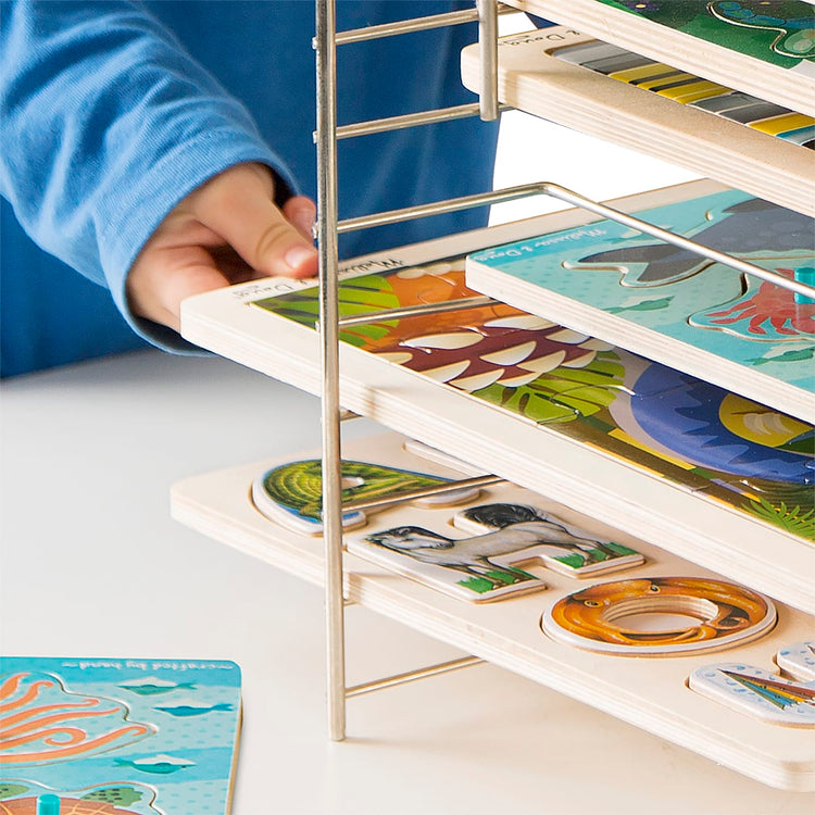 A child on white background with the Melissa & Doug Deluxe Metal Wire Puzzle Storage Rack for 12 Small and Large Puzzles