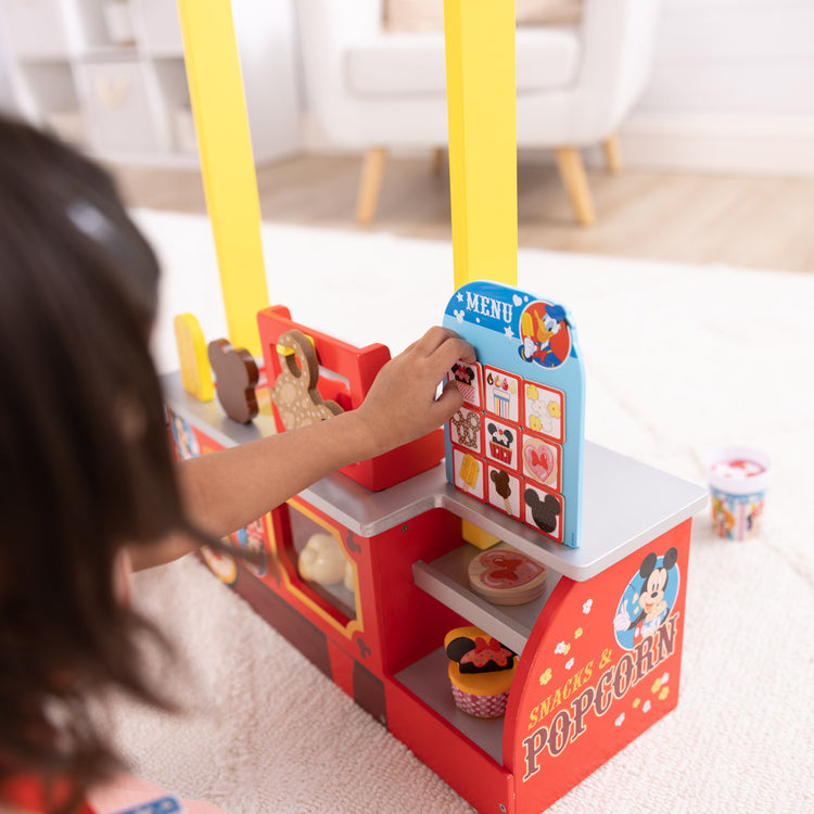 A kid playing with The Melissa & Doug Disney Snacks & Popcorn Wooden Pretend Play Food Counter – 33 Pieces