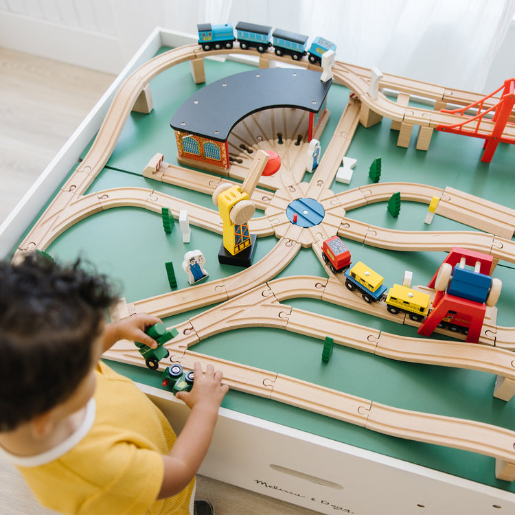 A kid playing with The Melissa & Doug Deluxe Wooden Railway Train Set (130+ pcs)