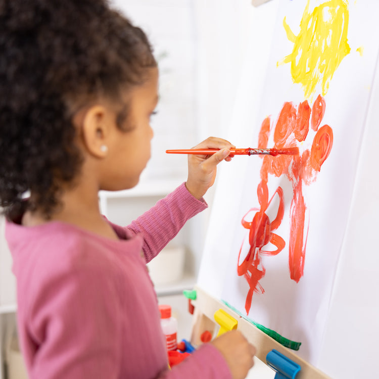 A kid playing with The Melissa & Doug Deluxe Standing Art Easel - Dry-Erase Board, Chalkboard, Paper Roller