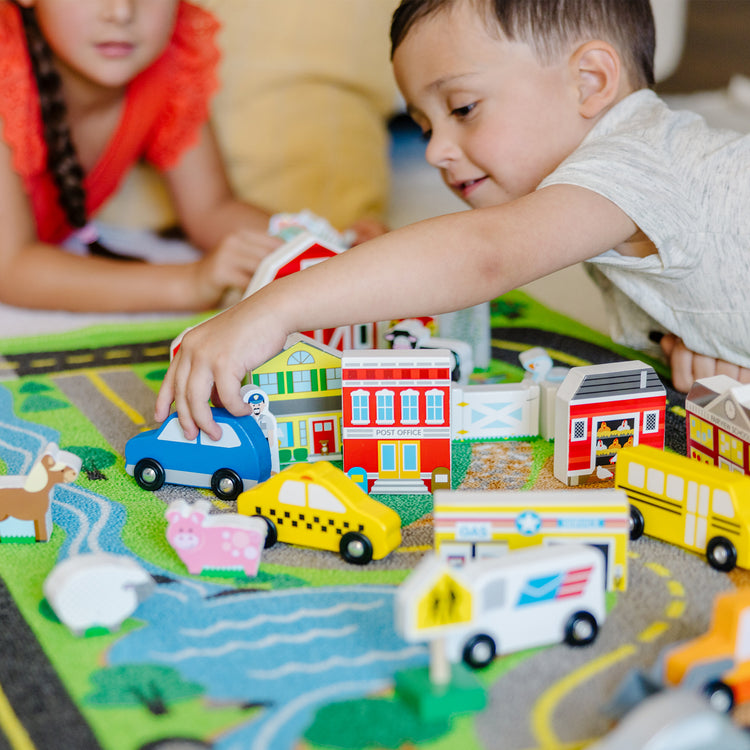 A kid playing with The Melissa & Doug Deluxe Activity Road Rug Play Set with 49 Wooden Vehicles and Play Pieces