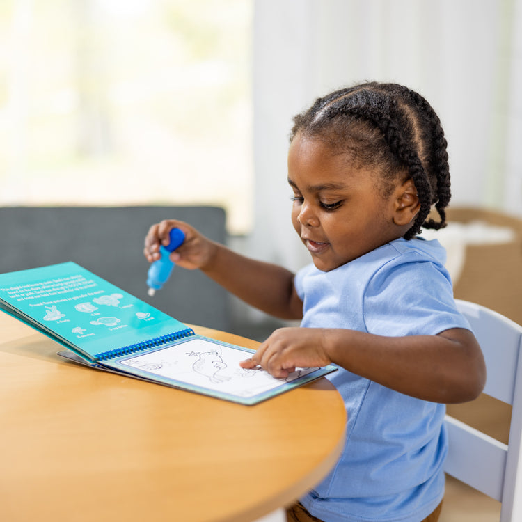 A kid playing with The Melissa & Doug On the Go Water Wow! Reusable Water-Reveal Activity Pad - Under the Sea