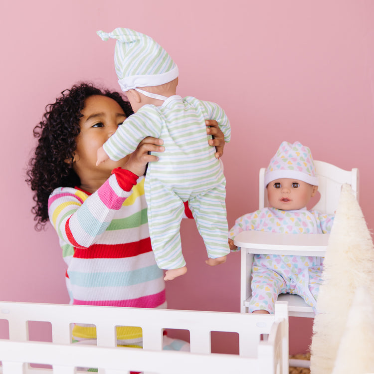 A kid playing with The Melissa & Doug Mine to Love Twins Sebastian & Sofia 15” Medium Skin-Tone Boy and Girl Baby Dolls with Rompers, Caps, Pacifiers