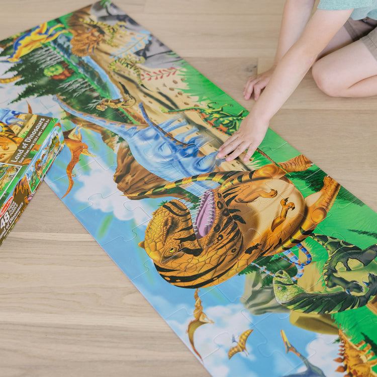 A kid playing with The Melissa & Doug Land of Dinosaurs Floor Puzzle (48 pcs, 4 feet long)