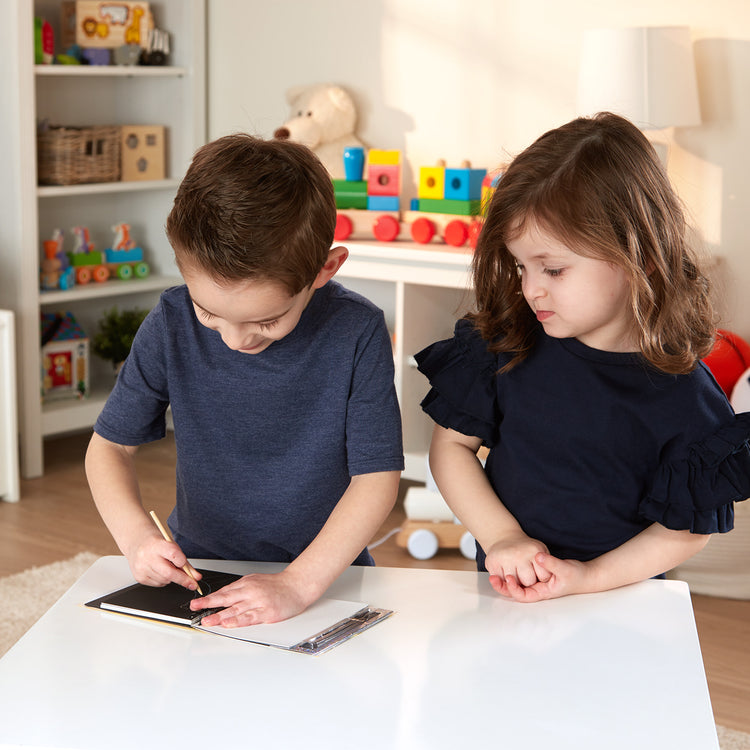 A kid playing with The Melissa & Doug Scratch Art Doodle Pad With 16 Scratch-Art Boards and Wooden Stylus