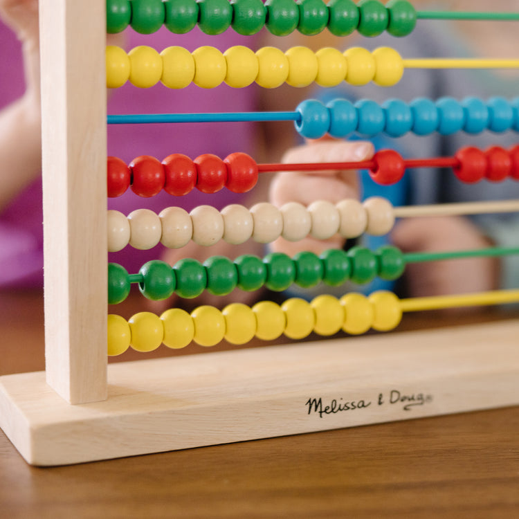 A kid playing with The Melissa & Doug Abacus - Classic Wooden Educational Counting Toy With 100 Beads