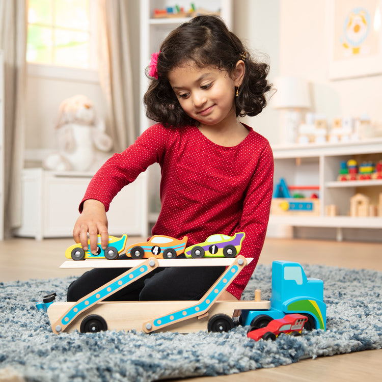 A kid playing with The Melissa & Doug Mega Race-Car Carrier - Wooden Tractor and Trailer With 6 Unique Race Cars