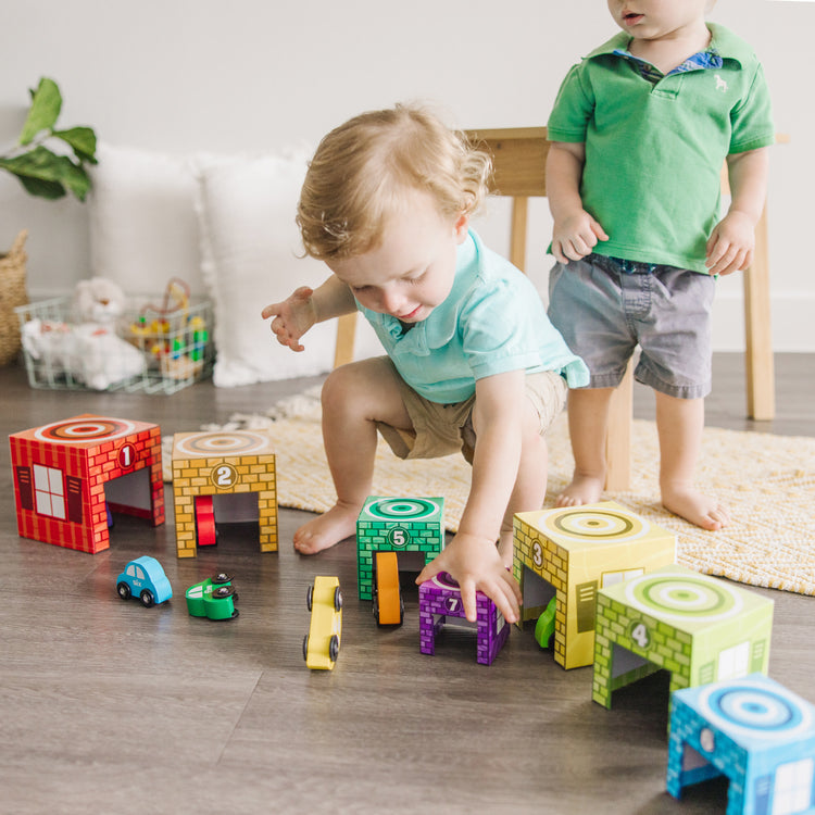 A kid playing with The Melissa & Doug Nesting and Sorting Garages and Cars With 7 Graduated Garages and 7 Stackable Wooden Cars