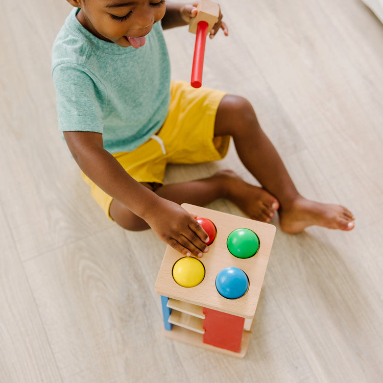 A kid playing with The Melissa & Doug Deluxe Pound and Roll Wooden Tower Toy With Hammer