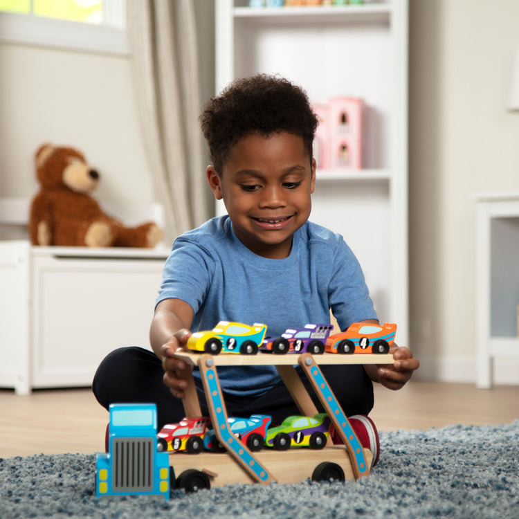 A kid playing with The Melissa & Doug Mega Race-Car Carrier - Wooden Tractor and Trailer With 6 Unique Race Cars