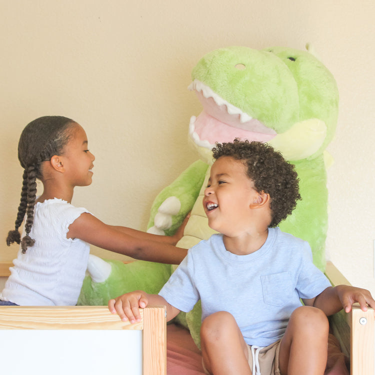 A kid playing with The Melissa & Doug Gentle Jumbos Dinosaur Giant Stuffed Plush Animal (Sits Nearly 3 Feet Tall)