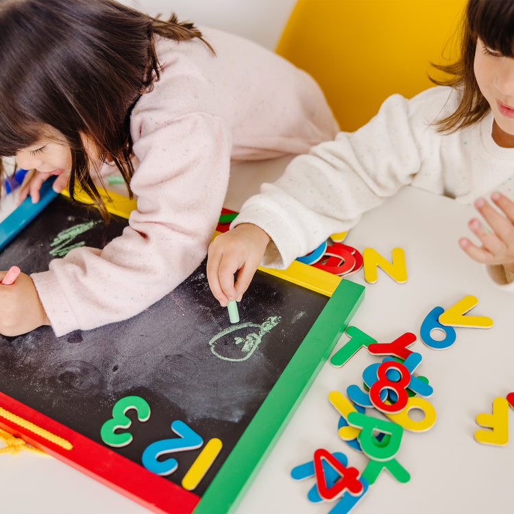 A kid playing with The Melissa & Doug Magnetic Chalkboard and Dry-Erase Board With 36 Magnets (Numbers and Uppercase Letters), Chalk, Eraser, and Dry-Erase Pen