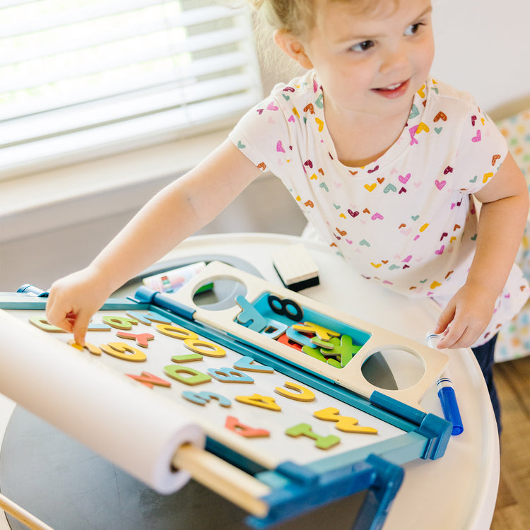 A kid playing with The Melissa & Doug Double-Sided Magnetic Tabletop Art Easel - Dry-Erase Board and Chalkboard