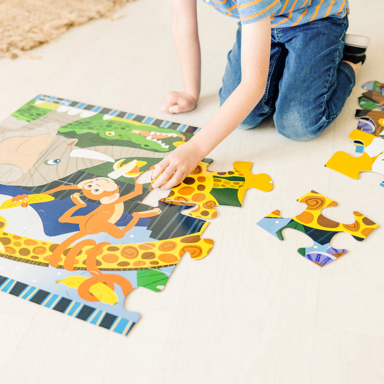 A kid playing with The Melissa & Doug Safari Social Jumbo Jigsaw Floor Puzzle (24 pcs, 2 x 3 feet)