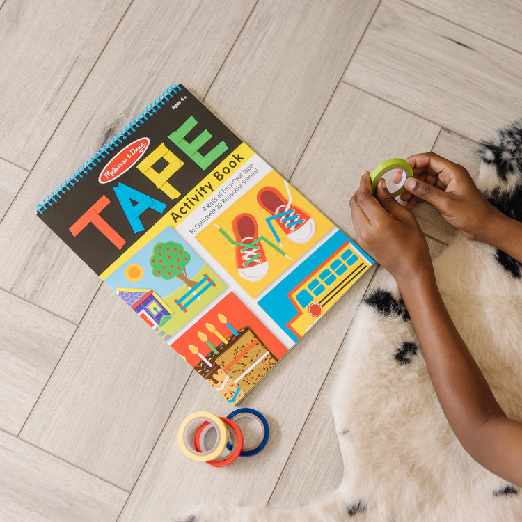 A kid playing with The Melissa & Doug Tape Activity Book: 4 Rolls of Easy-Tear Tape and 20 Reusable Scenes