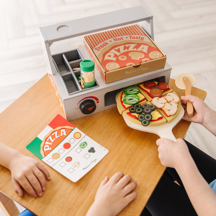 A kid playing with The Melissa & Doug Top & Bake Wooden Pizza Counter Play Set (41 Pcs)