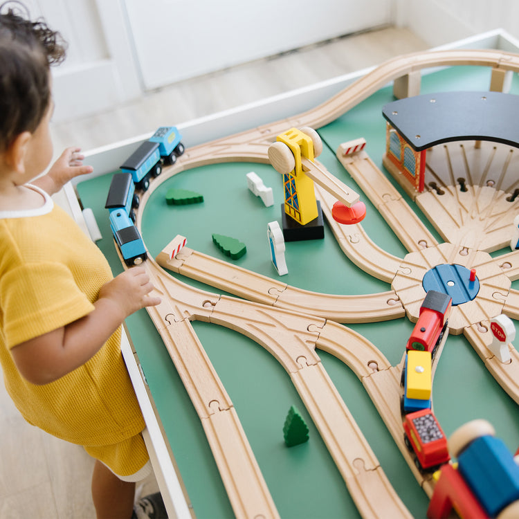 A kid playing with The Melissa & Doug Deluxe Wooden Railway Train Set (130+ pcs)