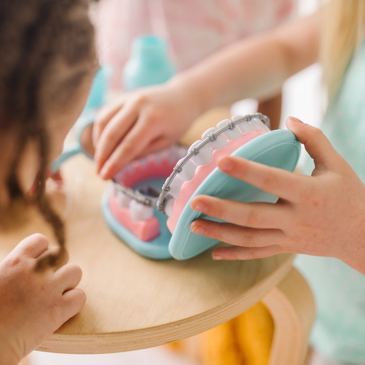 A kid playing with The Melissa & Doug Super Smile Dentist Kit With Pretend Play Set of Teeth And Dental Accessories (25 Toy Pieces)