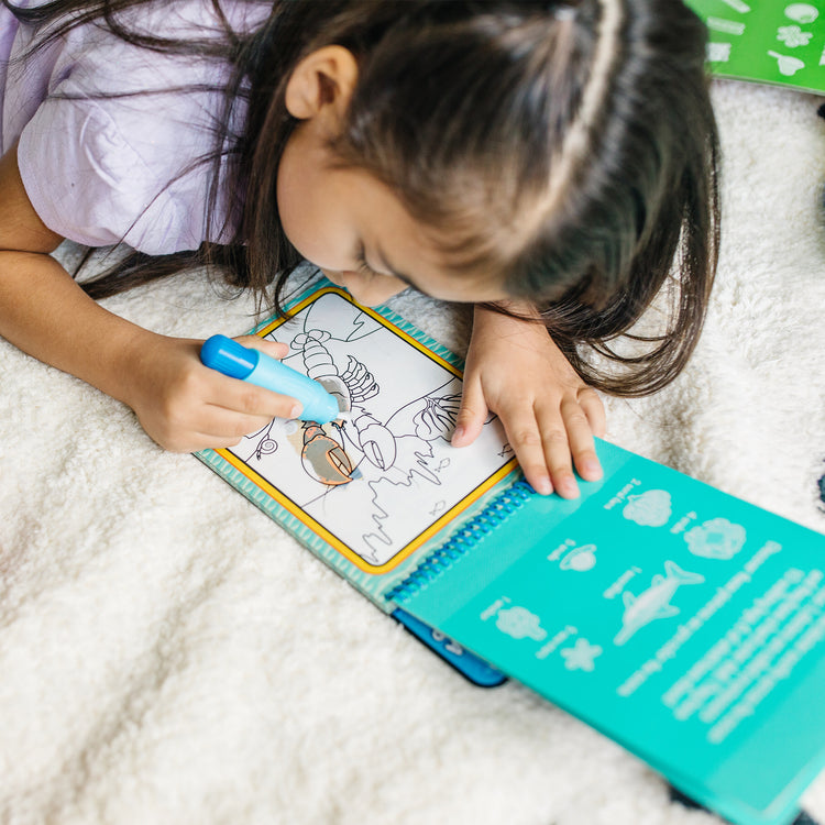 A kid playing with The Melissa & Doug On the Go Water Wow! Reusable Water-Reveal Activity Pad - Under the Sea