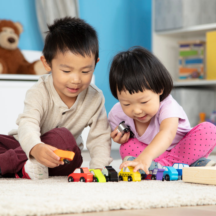 A kid playing with The Melissa & Doug Wooden Cars Vehicle Set in Wooden Tray - 9 Pieces