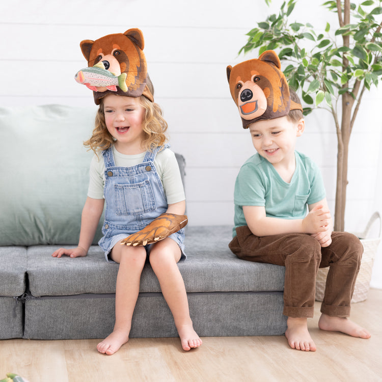 A kid playing with The Melissa & Doug Yellowstone National Park Grizzly Bear Games and Pretend Play Set with Plush Bear Heads and Bear Paw Gloves