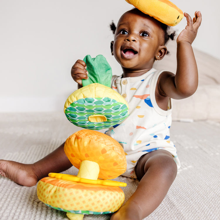 A kid playing with The Melissa & Doug Multi-Sensory Pineapple Soft Stacker Infant Toy