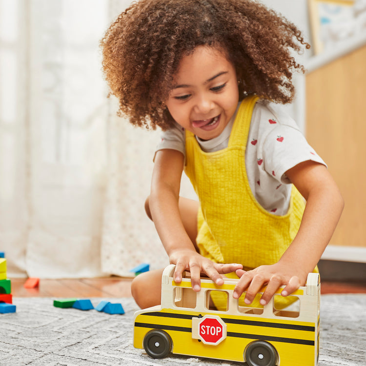 A kid playing with The Melissa & Doug School Bus Wooden Play Set With 7 Play Figures