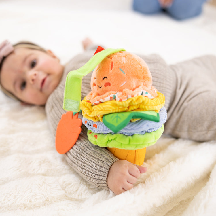 A kid playing with The Melissa & Doug Ice Cream Take-Along Clip-On Infant Toy with Sound and Vibration