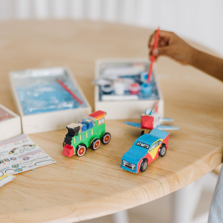 A kid playing with The Melissa & Doug Decorate-Your-Own Wooden Craft Kits 3-Pack - Plane, Train, and Race Car