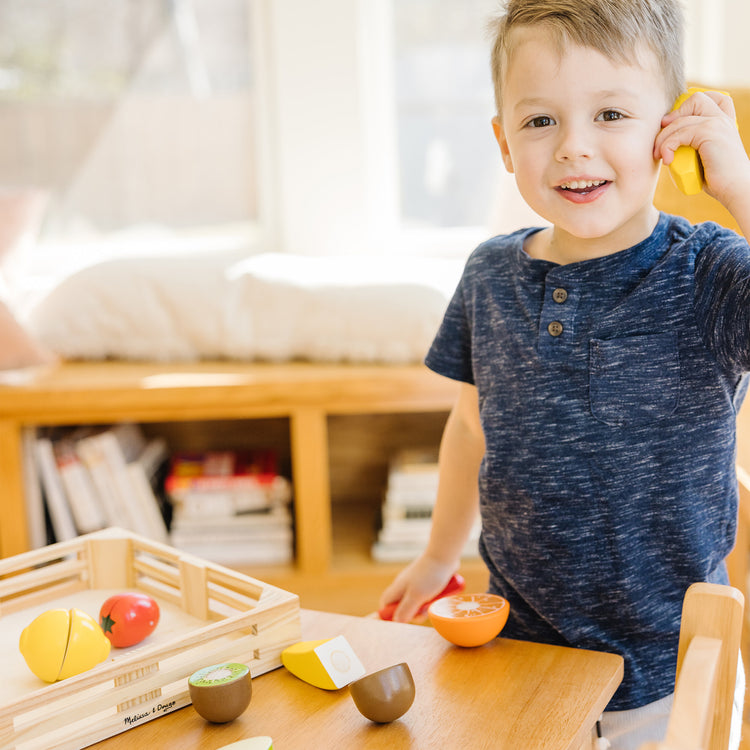 A kid playing with The Melissa & Doug Cutting Fruit Set - Wooden Play Food Kitchen Accessory, Multi