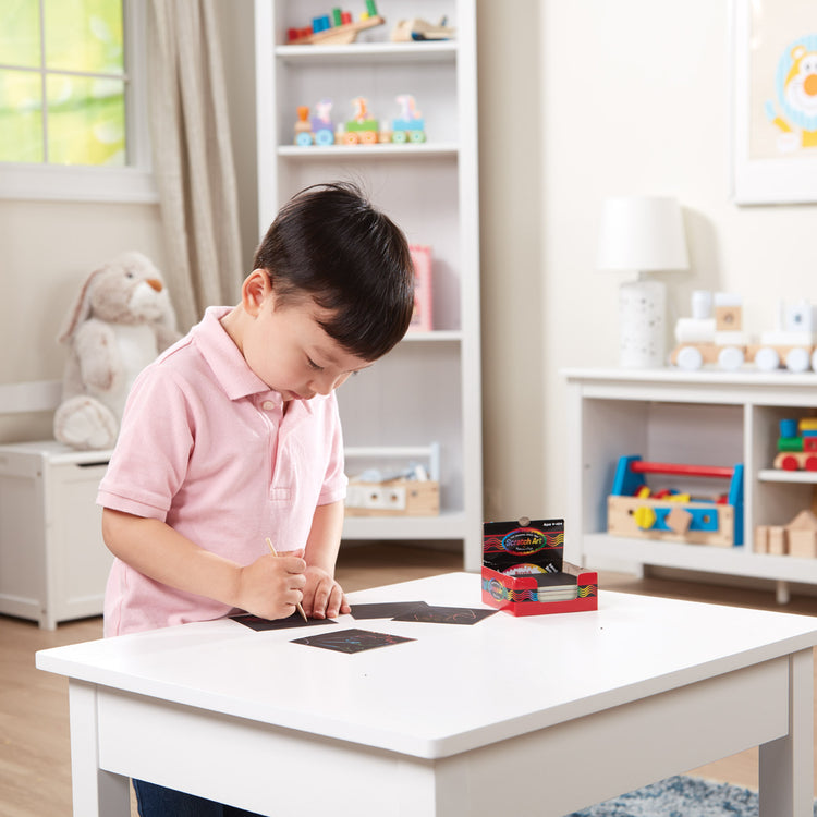 A kid playing with The Melissa & Doug Scratch Art Rainbow Mini Notes (125) With Wooden Stylus