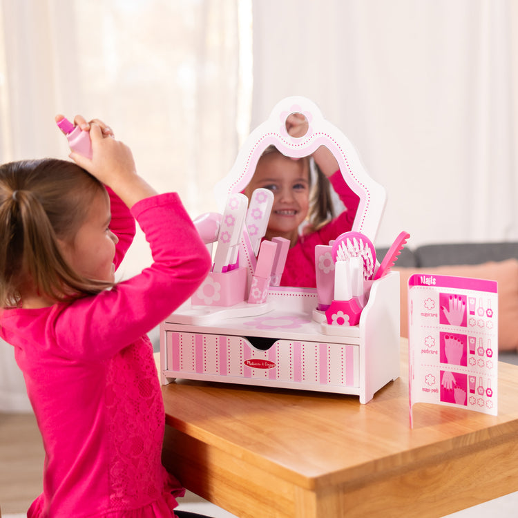 A kid playing with The Melissa & Doug Wooden Beauty Salon Play Set With Vanity and Accessories (18 pcs)