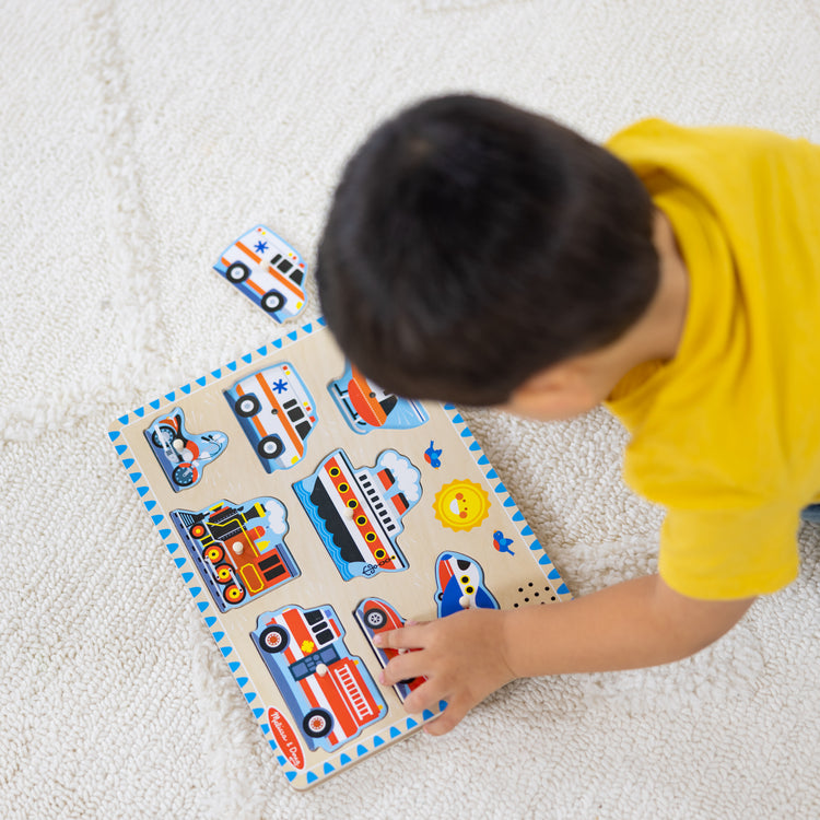 A kid playing with The Melissa & Doug Vehicles Sound Puzzle - Wooden Peg Puzzle With Sound Effects (8 pcs)